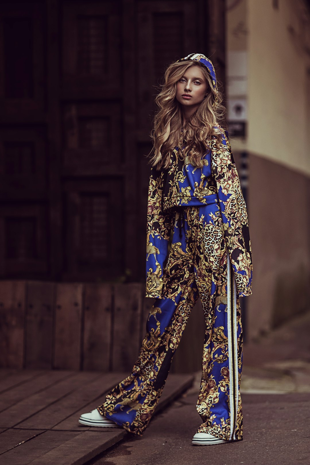 Stylish woman in ornate blue and gold tracksuit posing outdoors.